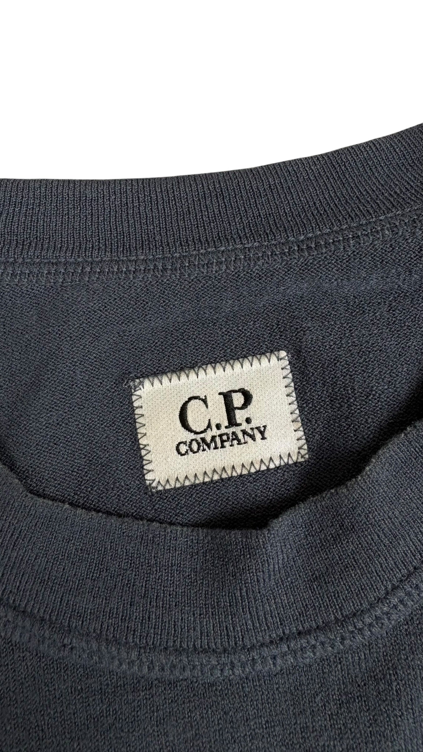 Gros plan sur l'etiquette tissee beige C.P Company cousue sur la poitrine du sweat bleu marine, vue detail