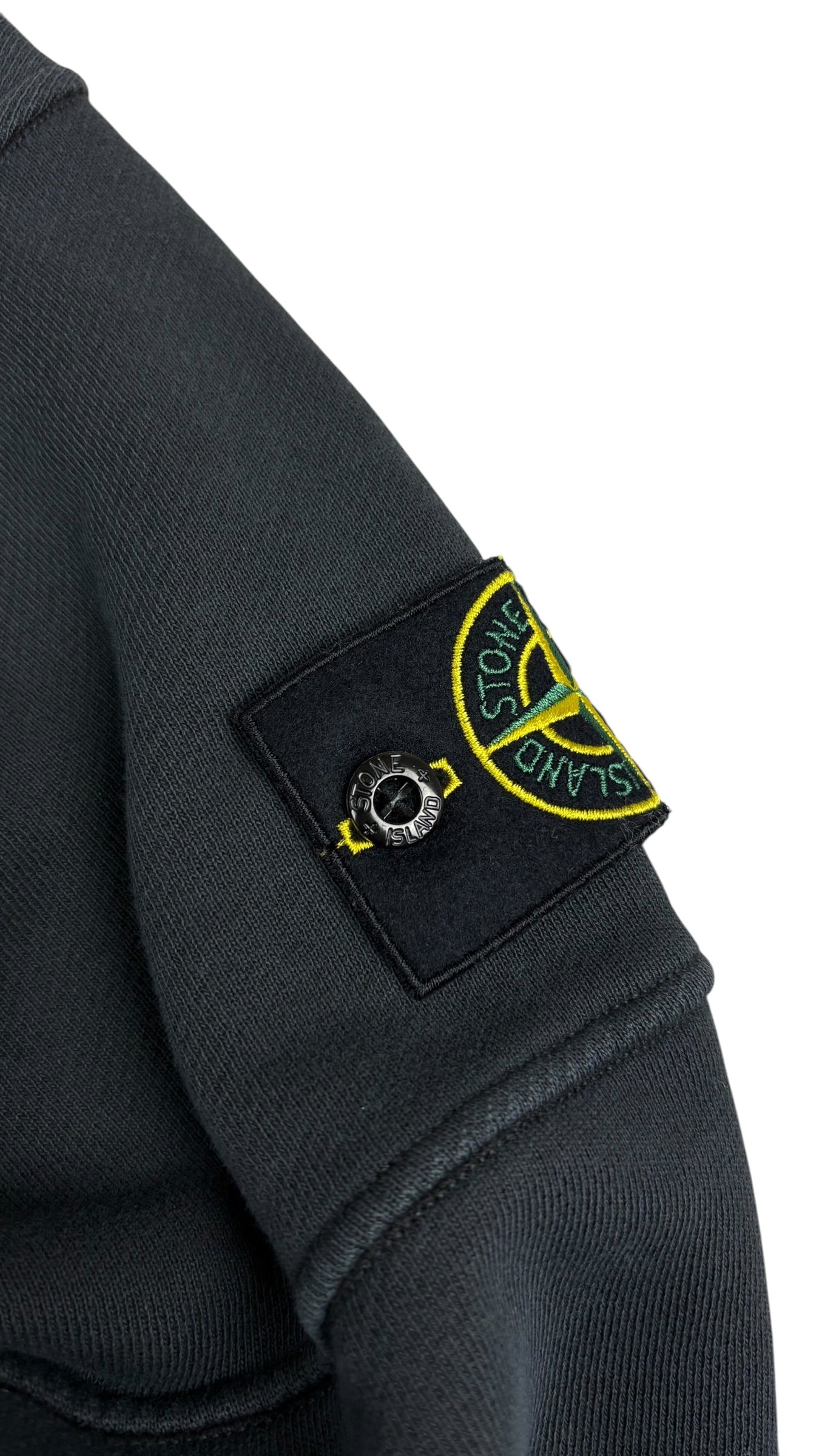 Gros plan du badge boussole Stone Island amovible fixé sur la manche gauche du crewneck gris