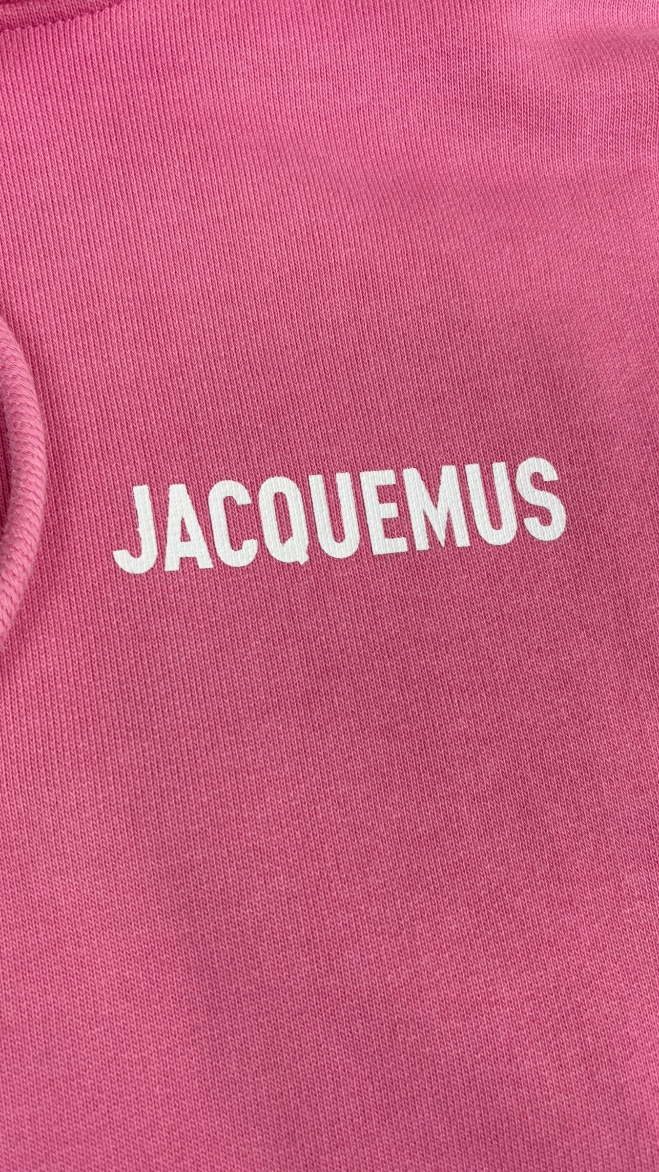Gros plan du logo Jacquemus blanc floqué sur la poitrine du hoodie rose