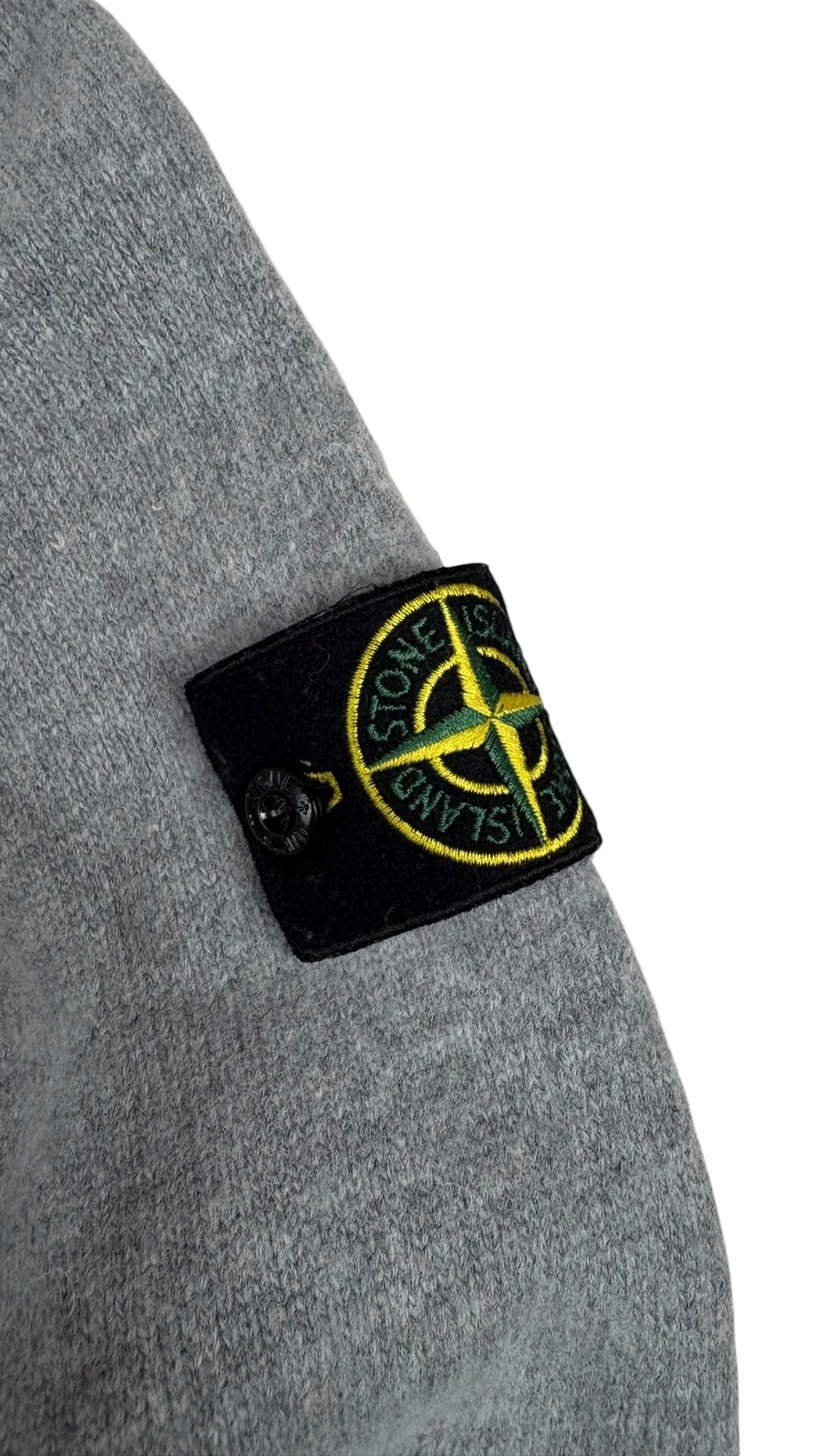Gros plan du badge boussole Stone Island fixé sur la manche gauche du pull gris
