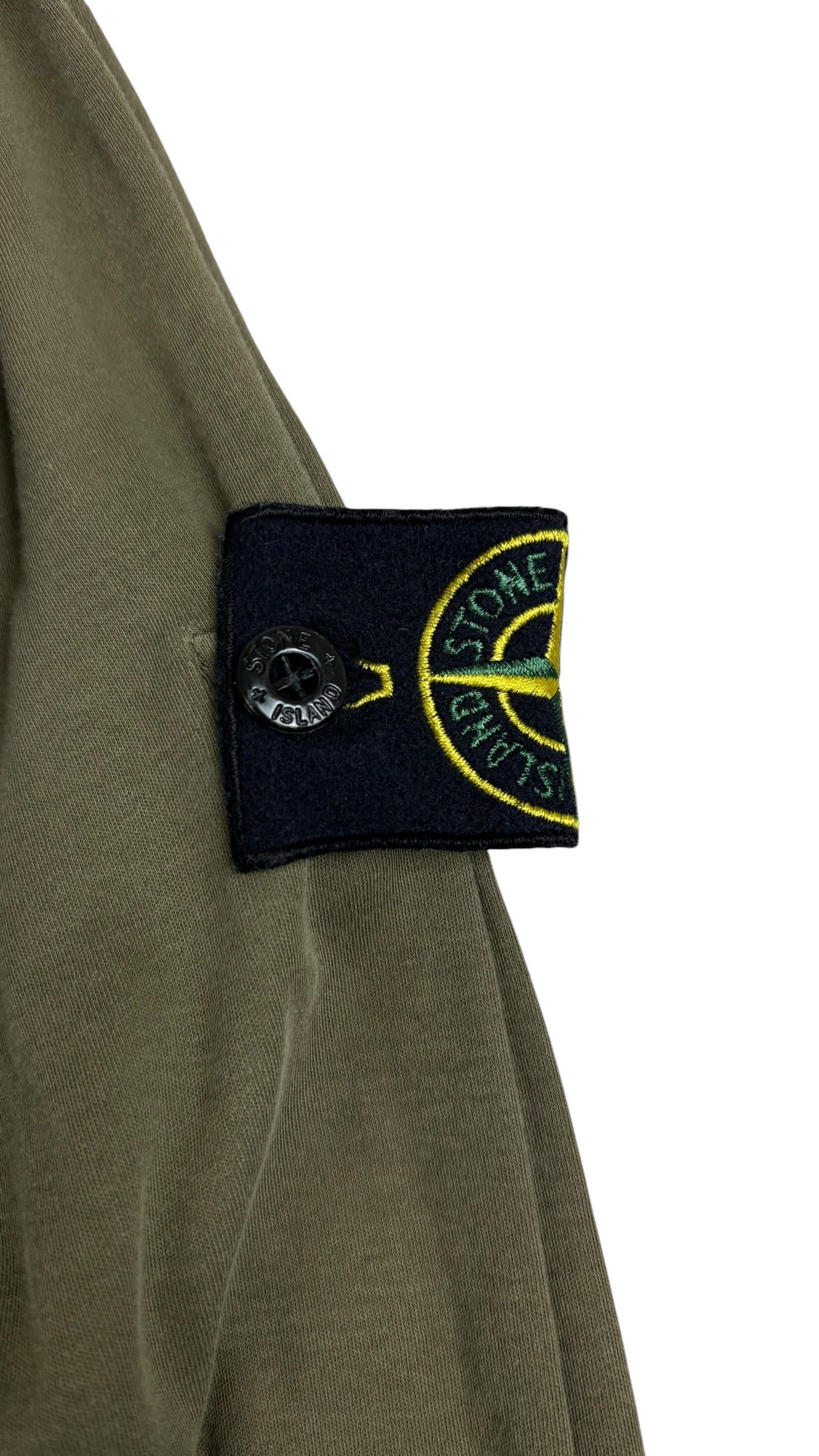 Gros plan du badge boussole Stone Island fixé par boutons-pression sur la manche du pull kaki