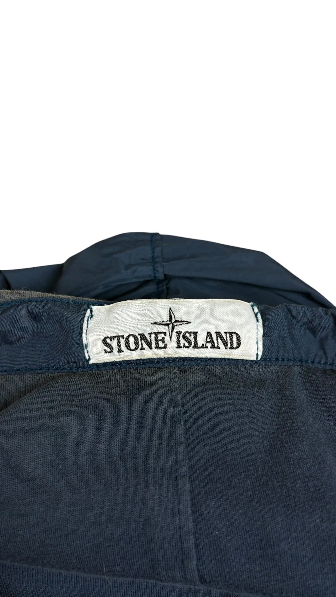 Gros plan sur l'étiquette de marque Stone Island tissée blanche avec le logo boussole, cousue à l'intérieur de la veste coupe-vent bleu marine, vue détail
