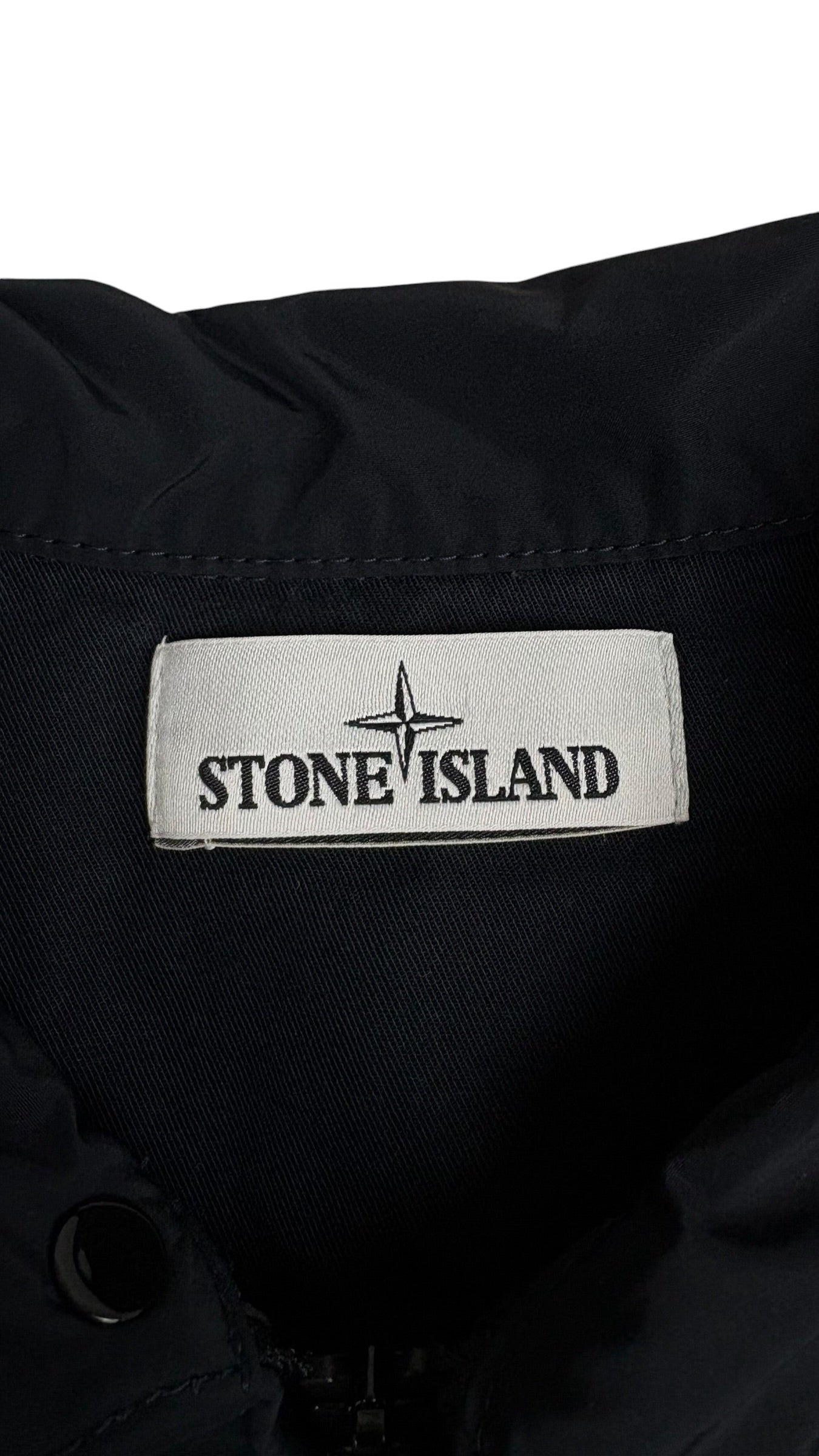 Gros plan sur l'étiquette de marque Stone Island tissée blanche avec le logo boussole, cousue à l'intérieur de la veste bleu marine, vue détail