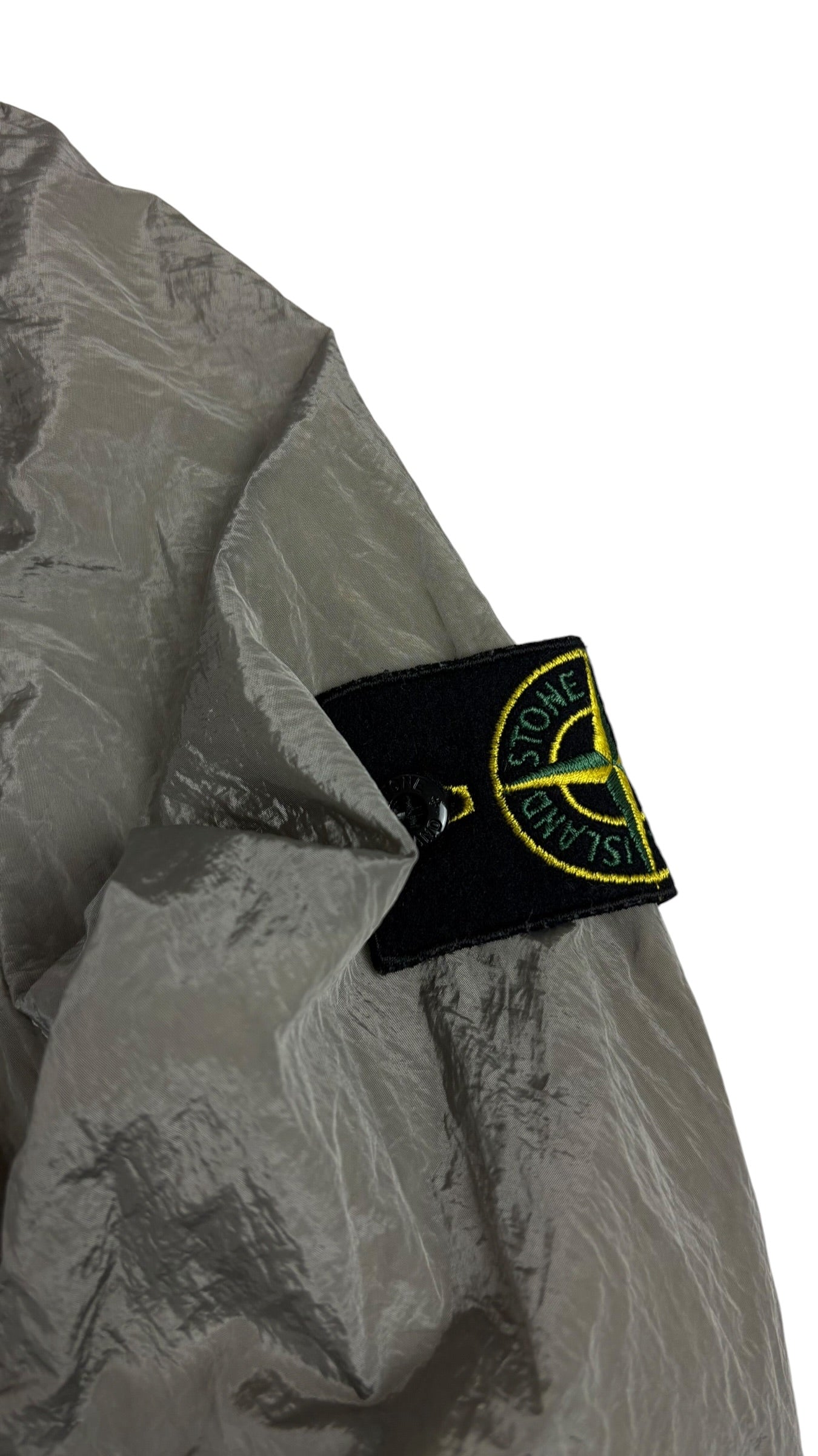 Gros plan sur le badge boussole Stone Island amovible fixé sur la manche de la veste en nylon métallisé