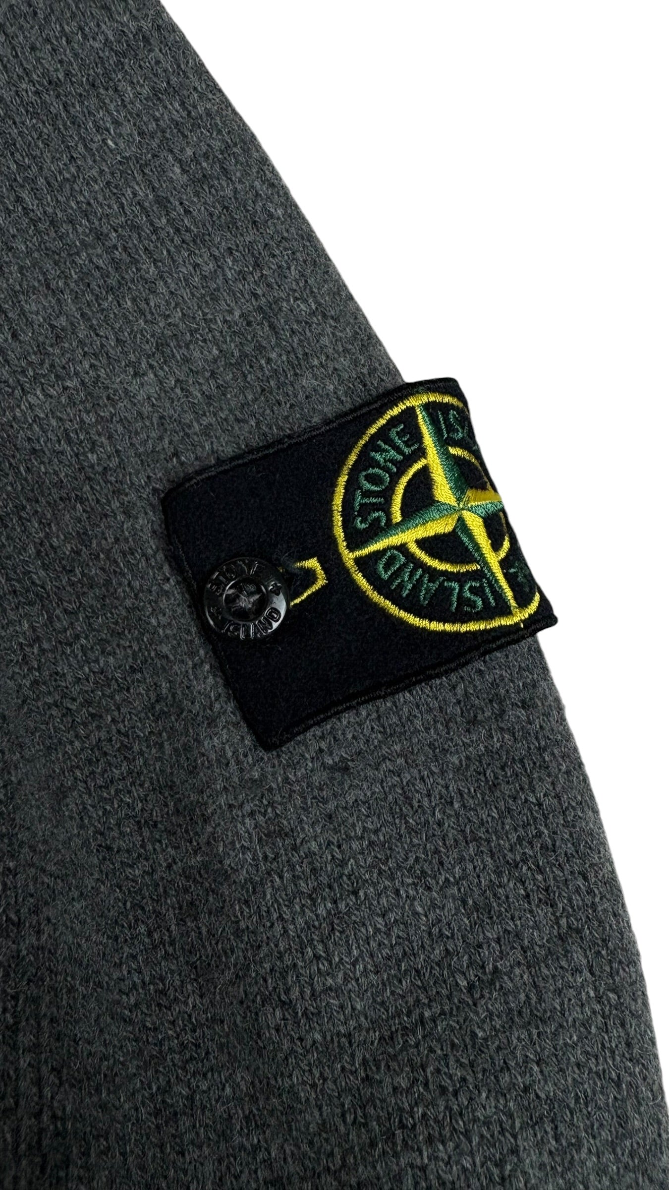Gros plan sur l ecusson Stone Island amovible fixe par bouton sur la manche gauche du cardigan gris