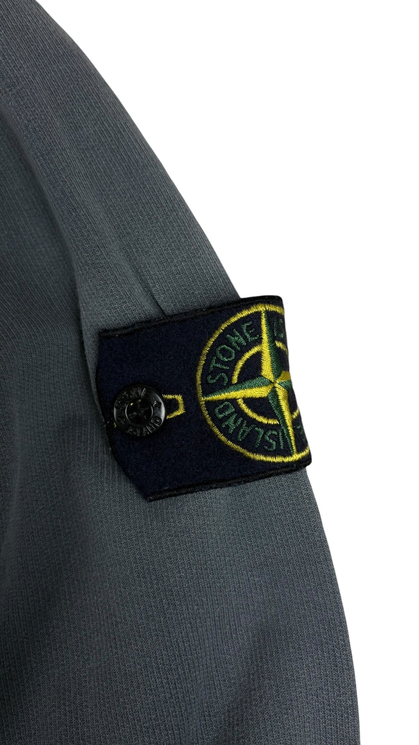 Gros plan sur l ecusson Stone Island amovible fixe par bouton sur la manche de la veste grise