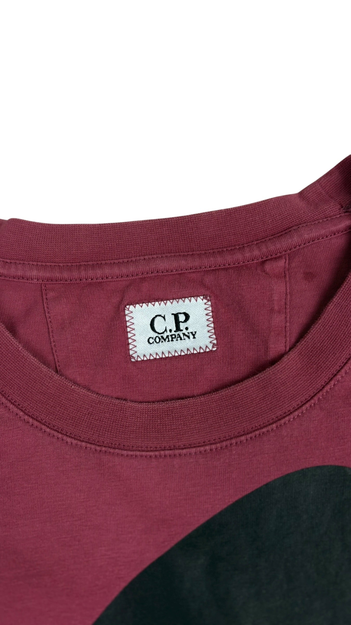 Gros plan sur l etiquette logo C.P Company cousue sous l encolure du tee-shirt bordeaux