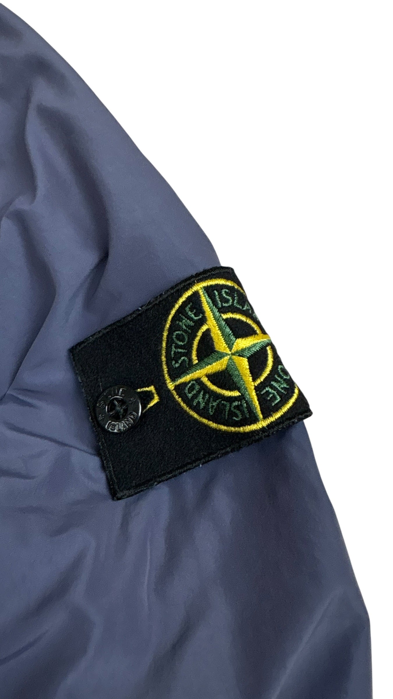 Gros plan du badge boussole Stone Island fixé sur la manche gauche de la veste bleu marine